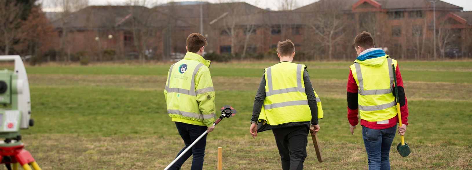 Three students in a field with engineering equipment