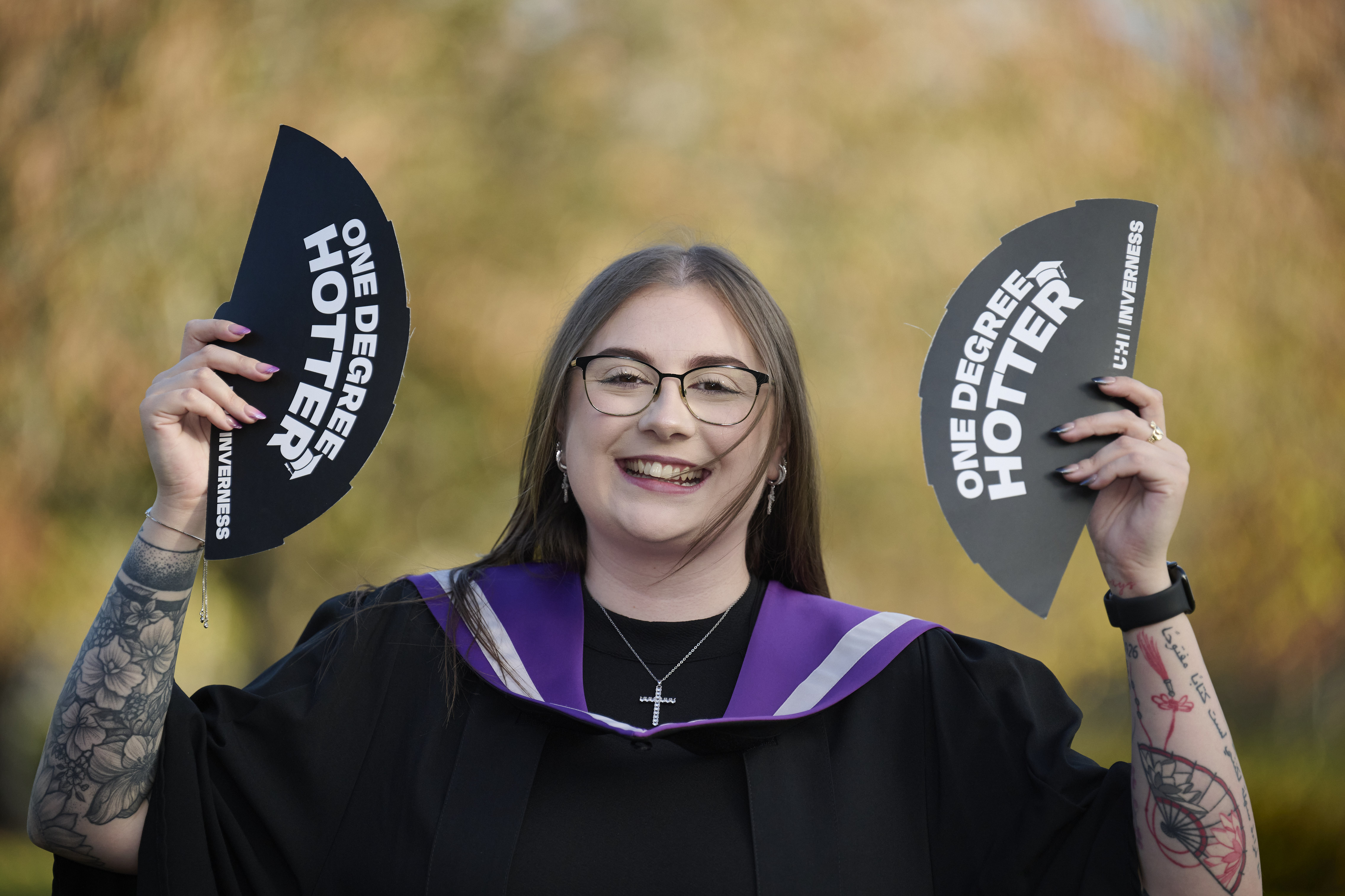 graduate in a gown holding up fans