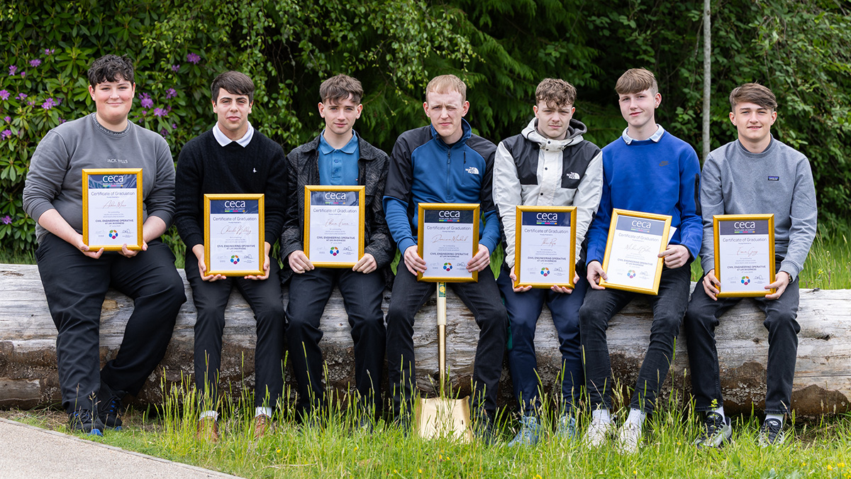 Seven male students sitting on a log holding certificates along with a golden shovel