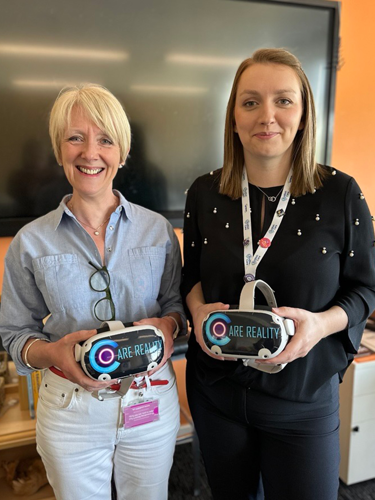 Two women standing in front of a TV screen holding headsets