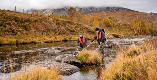 Two researchers in a river, sampling the water.