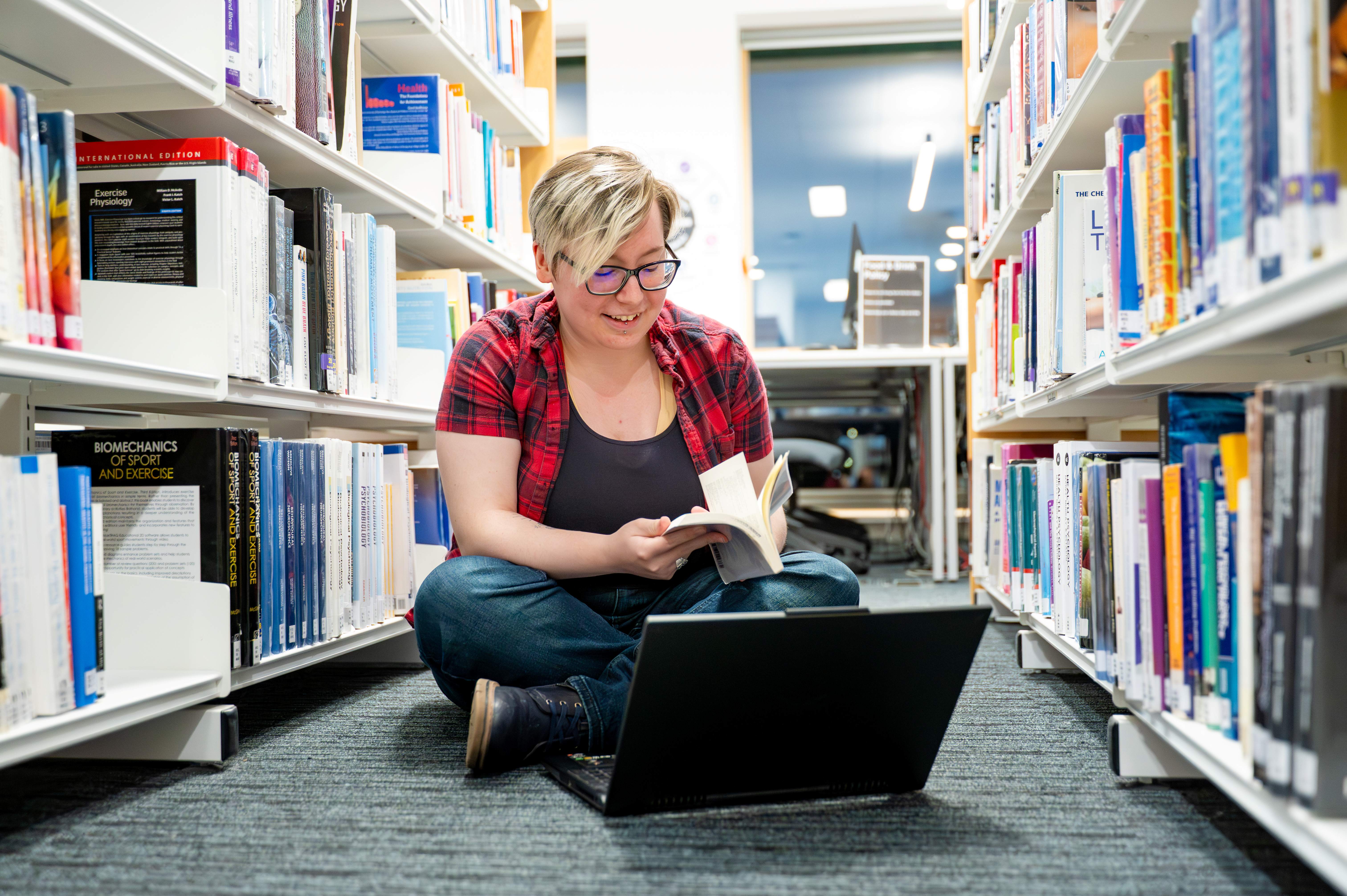 student sitting crossed legged on the floor, looking at a book