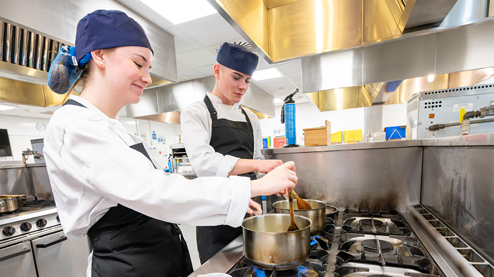 Two UHI Inverness professional cookery students preparing food in the campus professional kitchen