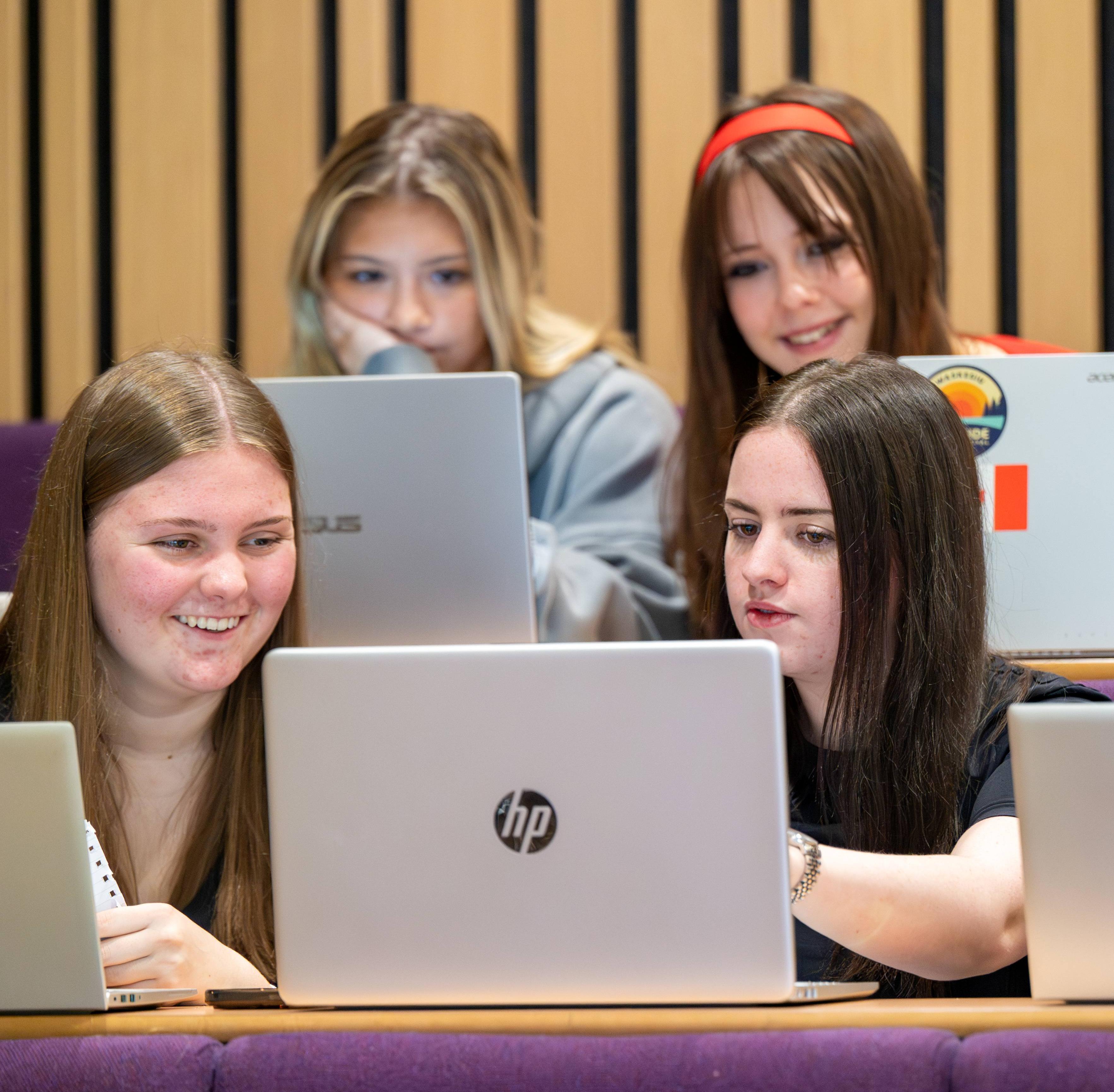 Four students looking at a laptop in a lecture theatre