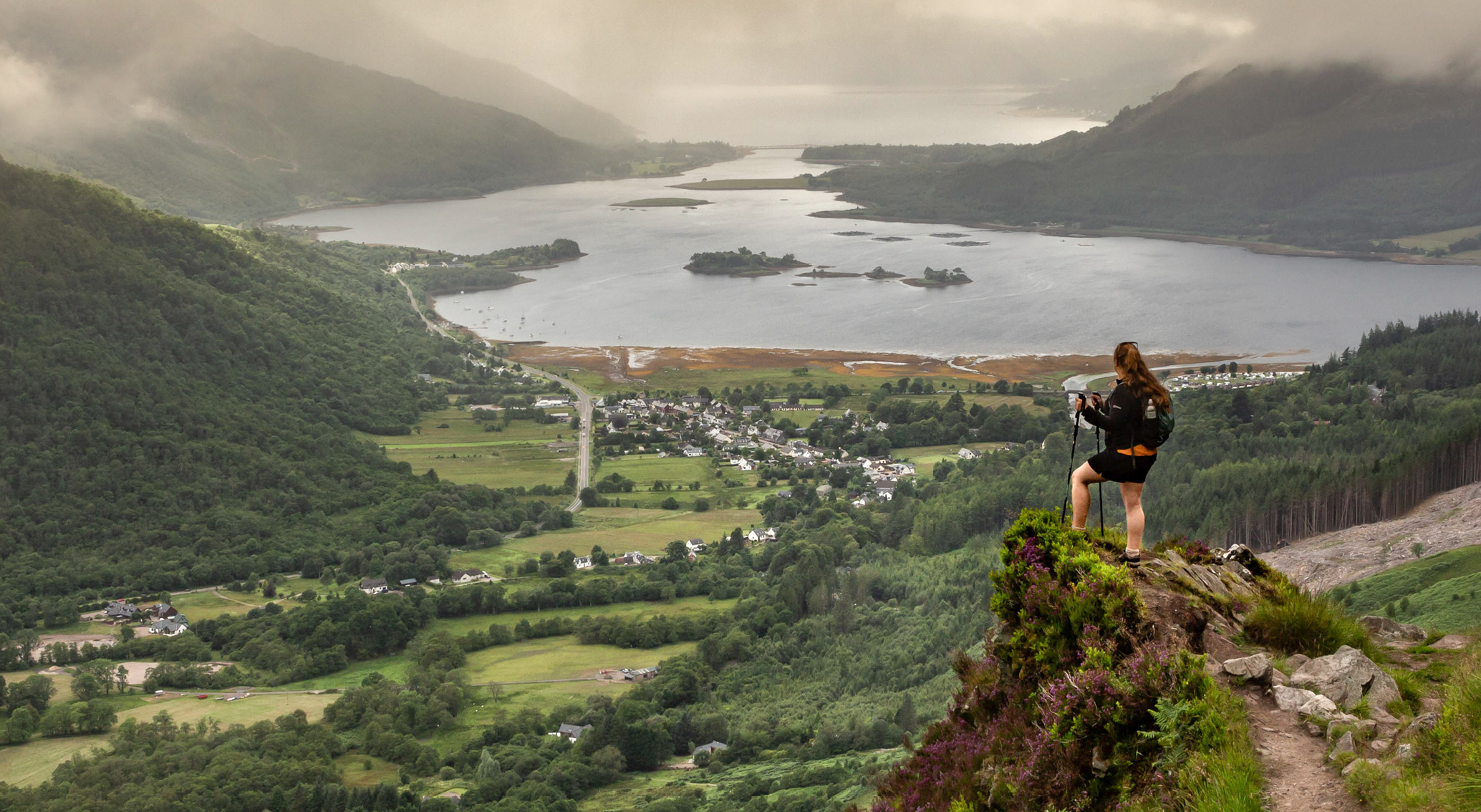 Woman standing on a rock with hiking poles overlooking Glencoe Woman standing on a rock with hiking poles overlooking Glencoe